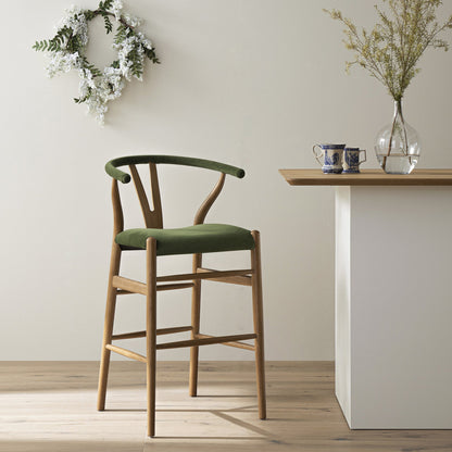Tabouret de bar rembourré Hansel, velours vert mousse et cadre en noyer clair